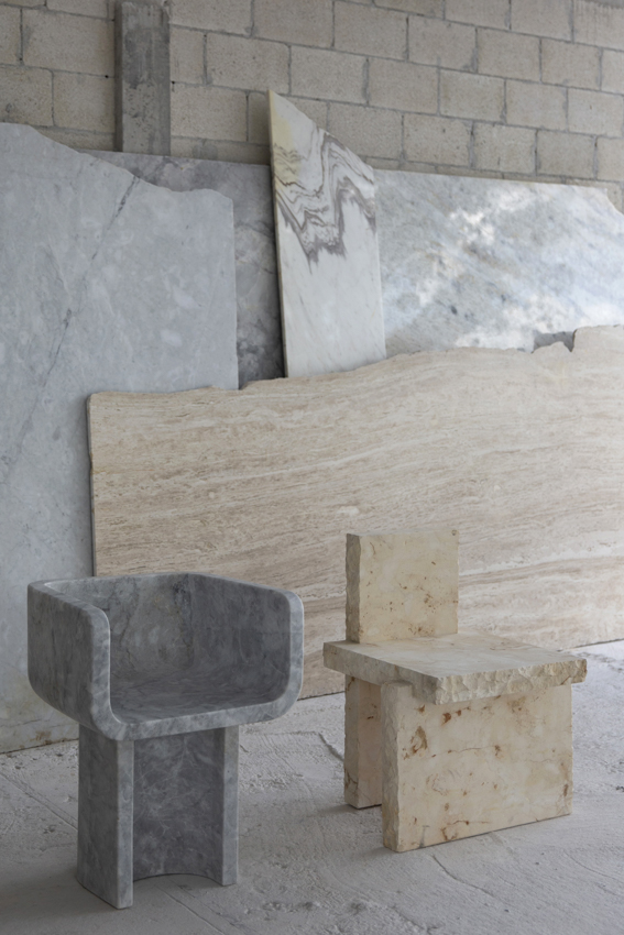 Chair 11 in grey marble beside Chair 20 in limestone, stone slabs behind