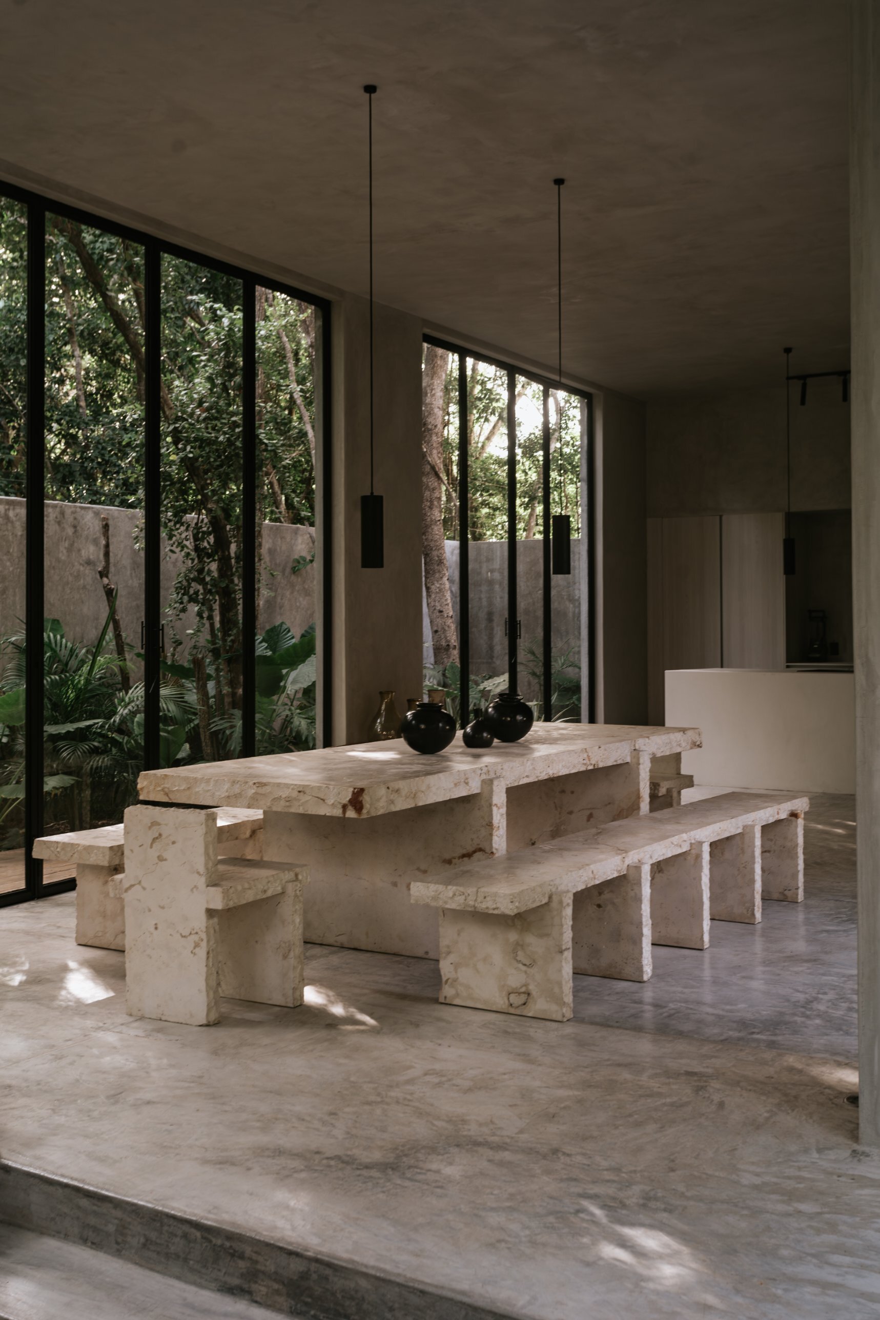 Table 20 with Bench 20 and Chair 20 beside floor-to-ceiling windows and garden, black vessels on the table