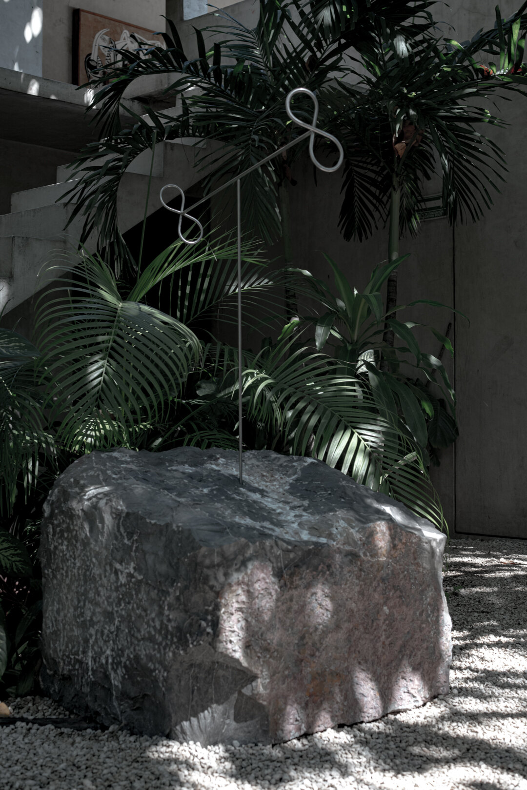 Sculpture I: a low, wide marble block among palms, steel loops above